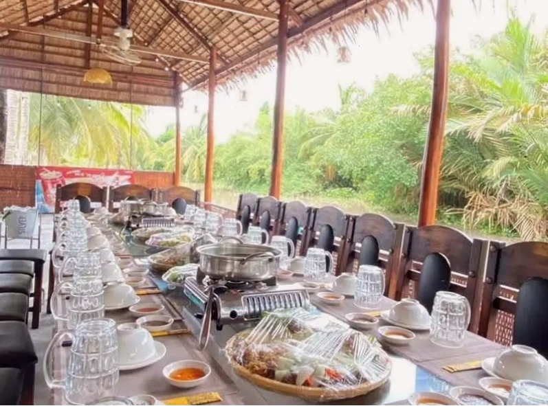Khu vực bàn ghế gỗ mộc mạc bên trong Nhà hàng Gió Sông Bến Tre