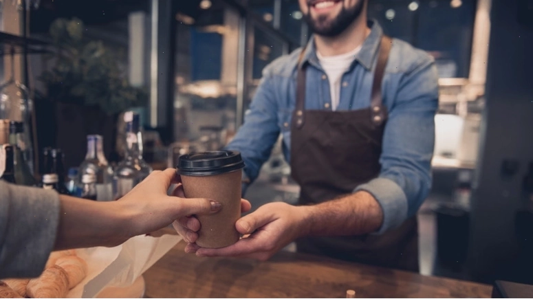 Nhân viên pha chế mỉm cười khi đưa cốc cafe mang đi cho khách hàng